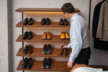 Young European man with dark hair brings wardrobe order puts everything in its place. Closet organized. Man chooses clothes. Capsule wardrobe for men.