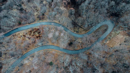 Aerial high angle view of narrow winding curvy mountain road among the trees in winter forest. Bird's eye view landscape.