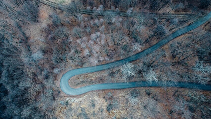 Aerial high angle view of narrow winding curvy mountain road among the trees in winter forest. Bird's eye view landscape.