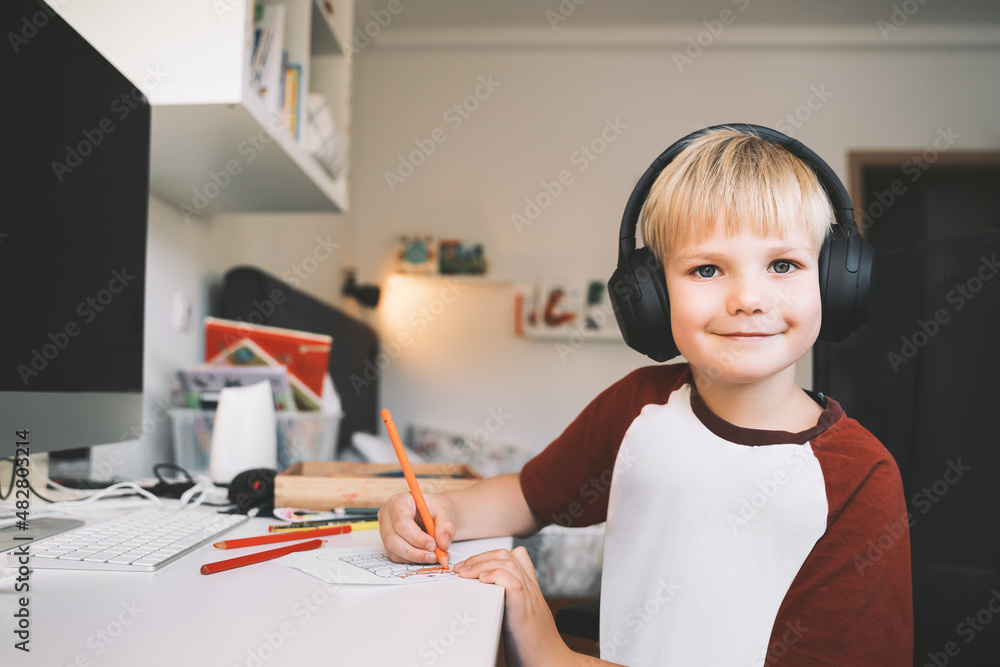 Wall mural Child 7 years old is homeschooling or distance online education. Elementary school boy studying, does homework or creating at desk.