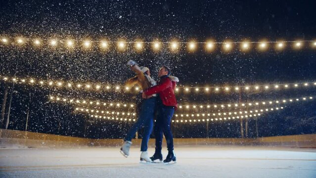 Romantic Winter Snowy Evening: Ice Skating Couple Having Fun on Ice Rink. Pair Skating Boyfrined Lifts His Beautiful Girlfriend and Spins. Love, Dance, Embrace, Figure Skate. Wide Slow Motion