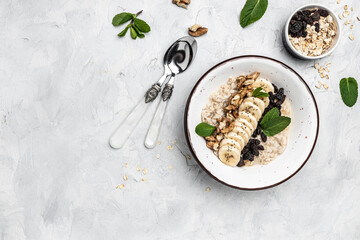 Oatmeal. Porridge with dried raisins, banana and walnuts decorated with mint for healthy breakfast or lunch. Natural ingredients. Clean eating, dieting, vegan food concept. top view
