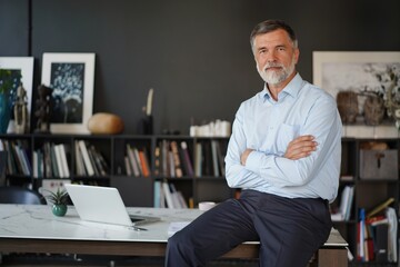 Portrait of happy successful businessman at work. Senior business man standing by office desk in...