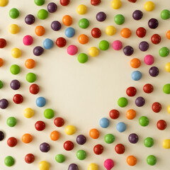 Heart or love symbol made with colorful candies. Minimal  Valentines or Mother's day concept against baige background.