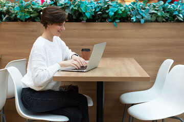 Young beautiful woman sitting at a shopping center at a table and working at a computer laptop. Freelance concept