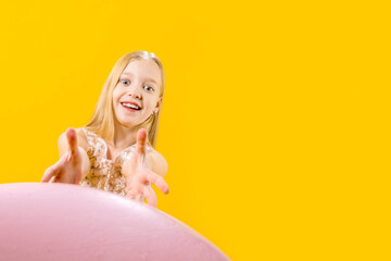 Obraz na płótnie Canvas Sweet gift. Round dessert. A cute girl in shock wants to take a huge pink macaroons on a yellow background. Christmas sweetness