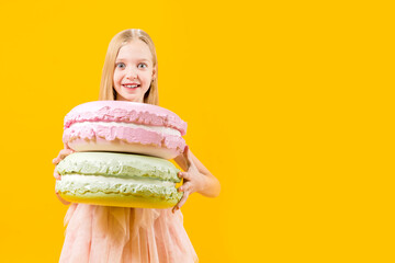 Sweet gift. A cute girl is holding two huge macaroons on a yellow background. Round dessert....