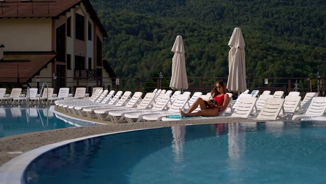 woman is resting in resort hotel in mountain in weekend, lying on lounge chair near swimming pool