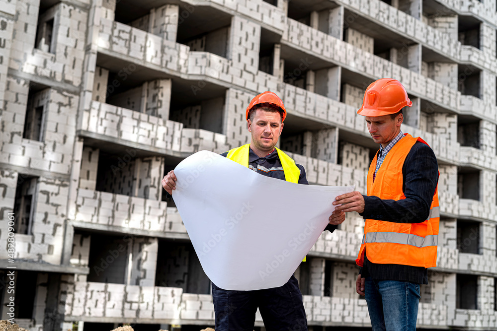 Wall mural two workers in helmet uniforms with construction plan standing on construction of houses