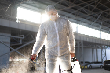Man dressed white protective overalls spraying surface antibacterial sanitizer sprayer during...