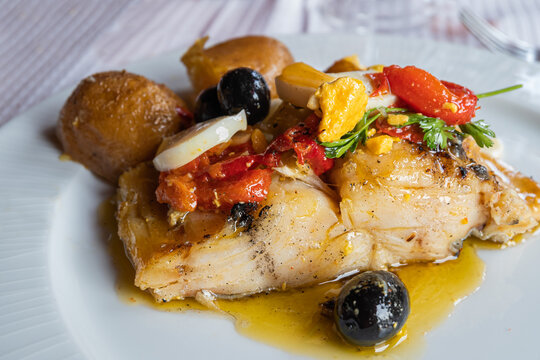 Closeup of a plate of good cod from the Atlantic sea with potatoes, onion, egg, red pepper, olives and coriander