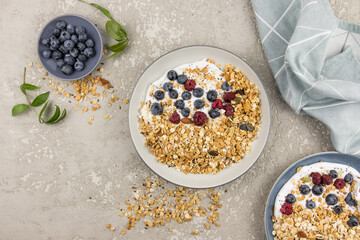 yogurt with homemade baked muesli and raspberries and blueberries in a plate on a gray concrete background. top view. delicious ,healthy breakfast.