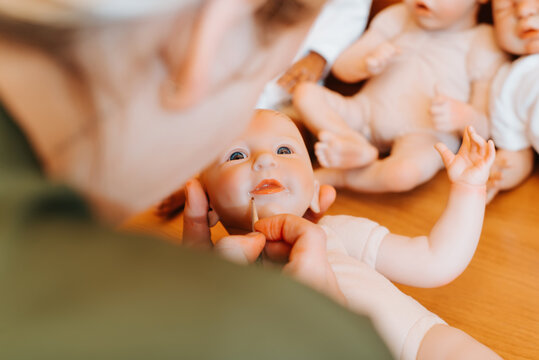 Close-up woman artist decorating cute realistic caucasian newborn baby doll with painting brush, lips design. Top view craftsman reborn in workshop, craft and hobby. Selective focus on brush and lips