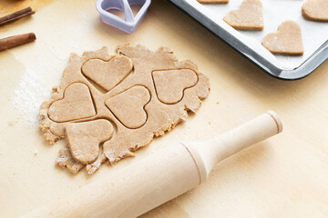 Cookies cut out in the shape of a heart with a rolling pin on a wooden background. The process of making holiday cookies for Valentine's Day. Home baking with love. Family care concept.