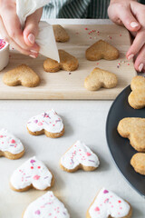 Women's hands decorate Ready cookies with icing. The process of making holiday cookies for Valentine's Day. Home baking with love. Vertical Orientation