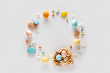 Easter composition in pastel colors. Round frame made of eggs, candies and flowers on a white background. Flat lay. Copy space