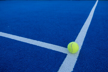 Paddle tennis ball on the line of a blue paddle tennis court.