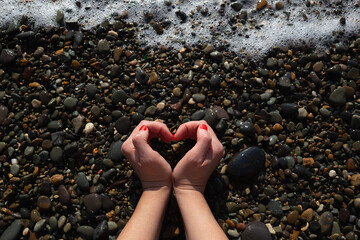 female hands depict a heart on the background of wet pebbles