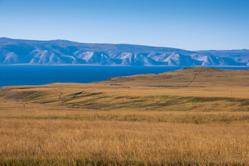 Fototapeta na wymiar Lake Baikal and mountains of Siberia with blue clear sky and yellow dry grass in autumn peaceful day, Russia Oklhon island