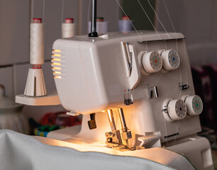 A white sewing machine with four spool threads and a lamp on the desktop. White overlock. Workplace concept.