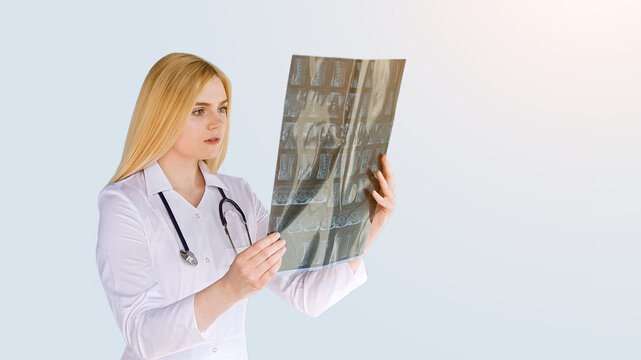 Healthcare, medicine concept: Portrait of young female doctor looking at x-ray isolated on gray background