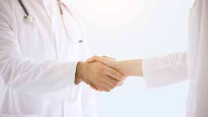 Healthcare, medicine concept: Doctors in lab coats greeting each other with handshake isolated over grey color background
