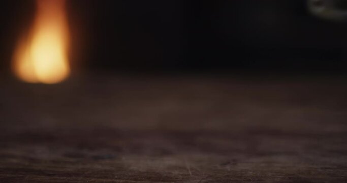 A man reaches for his near empty glass of Bourbon, then returns it to the table in front of the fireplace. 