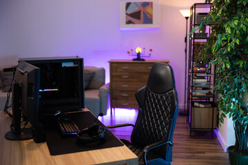 A backlit professional computer for a gamer. The monitor stands on a desk. The cozy room with modern design is lit with purple blue neon led lights. © ABCreative