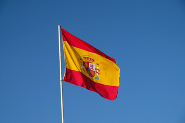 Spanish national flag waving on blue sky background. The flag on a flagpole flutters in the wind. Red with yellow Spain Flag blowing in the wind against on blue sky