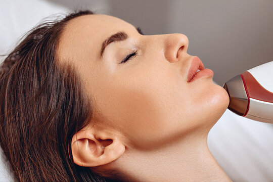 A close-up photo of a young female lying with closed eyes on white couch. Conducting rejuvenating procedure with a cosmetologist. Improving the quality of the skin. The concept of improving yourself.