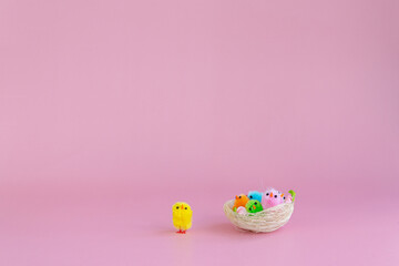 Decorative mini chickens of different colors on a pink background in a basket