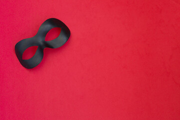 Black carnival mask on a light red background.