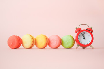 multi color of delicious sweet macaron and red analog alarm clock on pink background with copy space