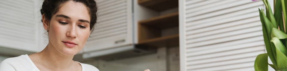 A woman holding a cut piece of something on a fork and looking at the phone in a kitchen