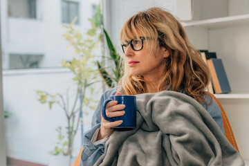 woman at home relaxed covered with blanket drinking coffee