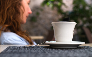 Close-up of a cup of hot coffee and a lonely girl in the background in blur. The girl sits alone in...