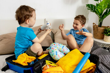 Two little boys with blue shirts ready for vacation. Happy children packing clothes into a suitcase...