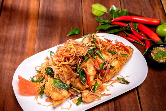 Thai fried fish with fish sauce and many herbs. A delicious recipe from southeast Asia and spices ingredients for cooking on wooden table background, Thai food, Asian foods, Thailand restaurant menu