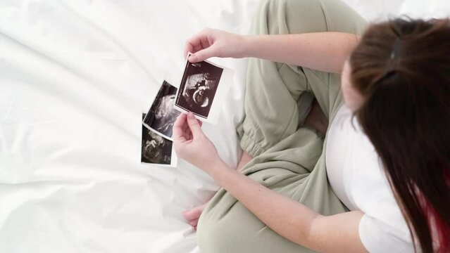 Top view cropped of pregnant woman looking ultrasound photo of fetus standing at home, young future mom waiting child first baby, pregnancy and motherhood concept