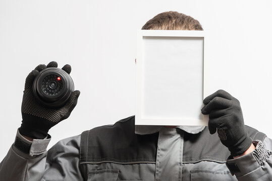 A Man With The Security Cctv Camera Is Hiding His Face Behind The Blank Photo Frame With Copy Space. Privacy Concept.