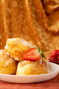 Portuguese malasada donuts sprinkled with sugar with strawberries on a fabric background in gold color vertical photo.