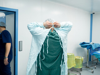 Rear view of the surgeon in the operating room removing the sterile operating gown at the end of the surgery. The surgeon undresses after surgery.