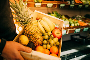 Person holding a basket of vegetables and fruits in the market.