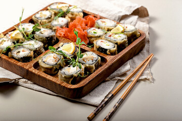 Hot sushi rolls. Baked rolls with shrimps on a wooden utensils. Bamboo chopsticks and soy sauce. Close-up. Copy space