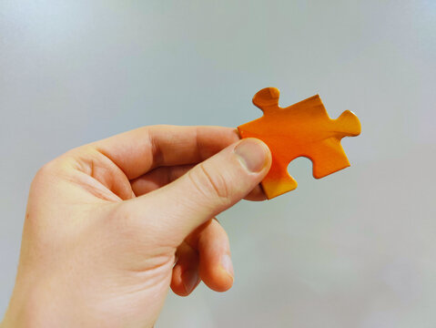 A Hand Holding A Single Orange Puzzle Piece