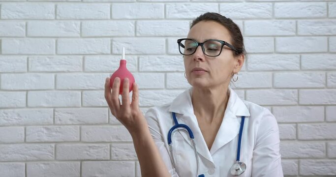 Pumping an enema. A curious woman doctor hold an enema in her hand.