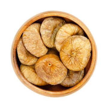 Dried figs in a wooden bowl. Sun dried, ripe and whole common figs, edible and uncooked fruits of Ficus carica, a popular snack in the wintertime. Close-up from above, isolated over white, food photo.