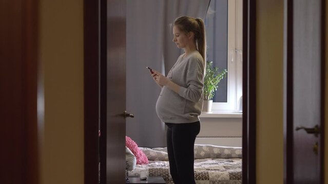 Young pregnant woman turns off her smartphone, undresses and goes to bed. She sent the last message of the day on her smartphone before going to sleep