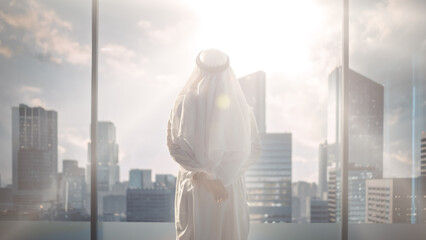 Successful Muslim Businessman in Traditional White Outfit Standing in His Modern Office Looking out of the Window on Big City with Skyscrapers. Successful Saudi, Emirati, Arab Businessman Concept.