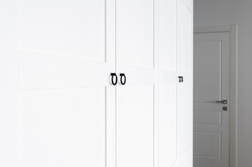 White wooden wardrobe with black handles. The interior of the apartment is in Scandinavian style